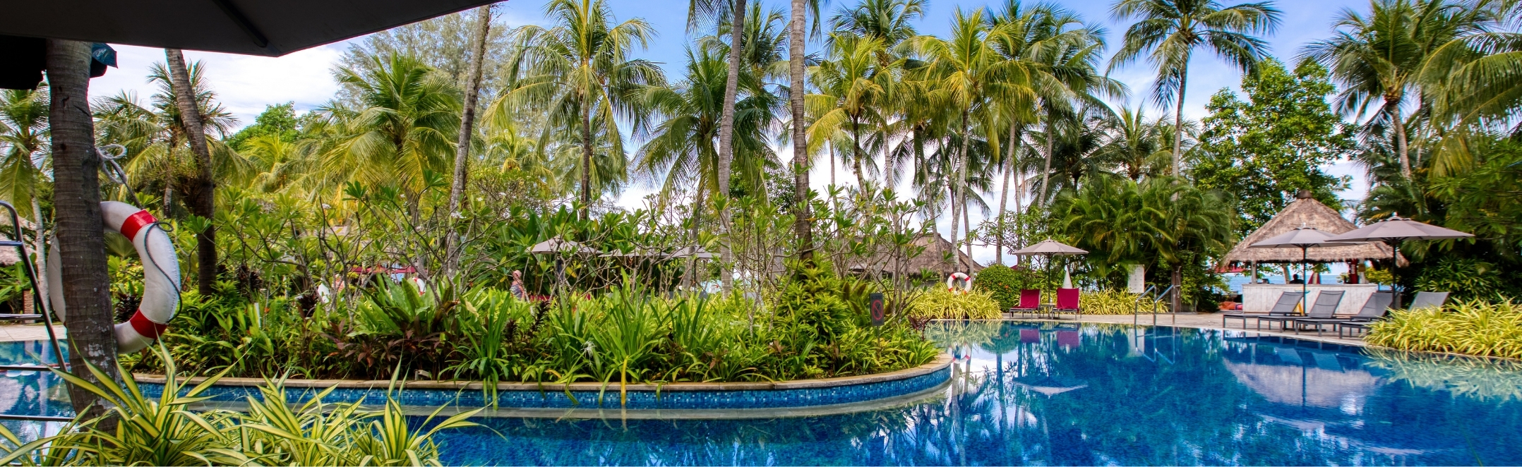 Lush palm trees frame the tranquil lagoon-style swimming pool at PARKROYAL Penang Resort's tropical beachfront retreat.